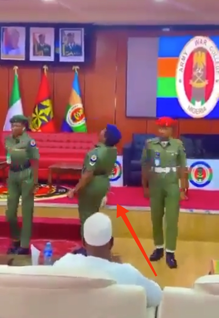A female Nigerian military officer collapsing during a parade, supported by a colleague.